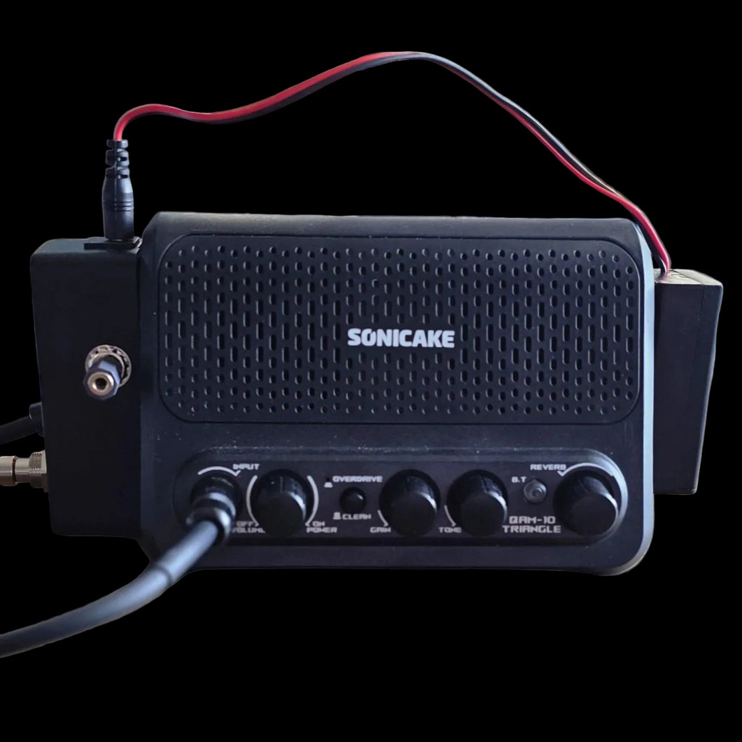Black Sonicake guitar amplifier on a black background with visible cables.