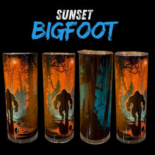 Four tall insulated tumblers with clear lids are shown against a black background, each printed with a spooky forest scene featuring a Bigfoot silhouette and glowing orange sunset tones. Large text at the top reads 'SUNSET BIGFOOT'.